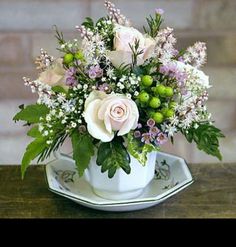 a white flower arrangement in a teacup on a saucer sitting on a table