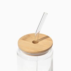 a glass jar with a wooden lid and a straw sticking out of the top, on a white background