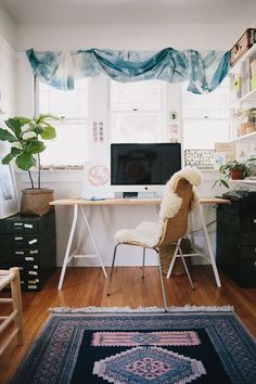 a desk with a computer on it in front of a window covered by blue drapes