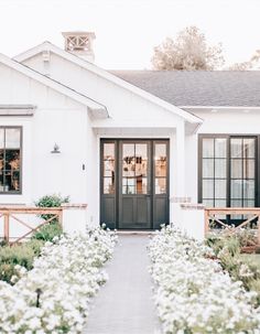 a white house with black doors and flowers in the front yard on a sunny day