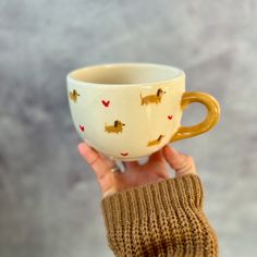 a person holding up a coffee cup with dogs on it and hearts painted on the side