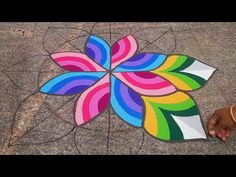 a person is standing next to a colorful flower design on the ground with their hands