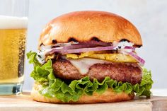 a hamburger with onions, lettuce and cheese next to a glass of beer