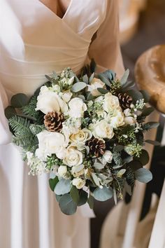 a bridal holding a bouquet of white flowers and pineconis in her hands