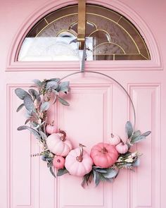 a pink front door with a wreath and pumpkins hanging on it's side