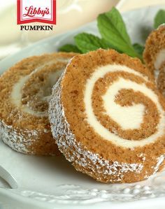 a roll is on a plate with powdered sugar sprinkled around it and green leaves