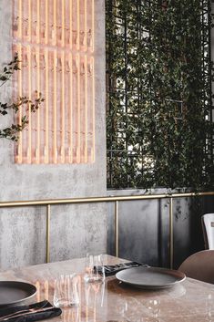 a table with plates and glasses on it in front of a wall covered with plants