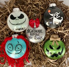 three glass ornaments with faces and words on them sitting in a pile of fake grass