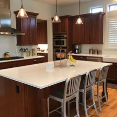 a large kitchen with wooden cabinets and white counter tops, along with two bar stools