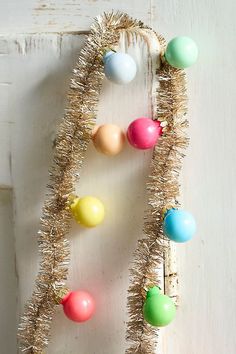 an assortment of colorful ornaments hanging on a white wooden wall with tinsele garland