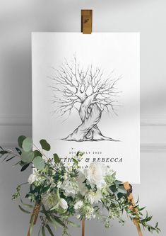 a white poster sitting on top of a easel next to flowers and greenery