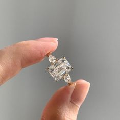 a woman's hand holding an engagement ring with two diamonds on it and one diamond in the middle