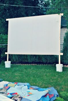 an outdoor projector screen sitting in the grass next to a blanket and potted plants