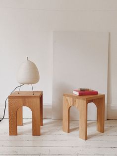 two wooden tables with books on them in front of a white wall and floor lamp