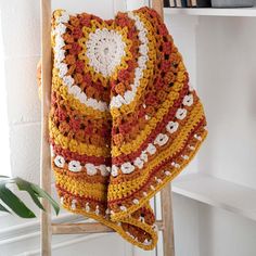 a crocheted blanket hanging on a ladder next to a potted plant and bookshelf