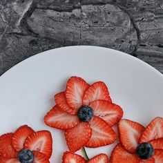 strawberries and blueberries are arranged on a white plate with some flowers in the middle