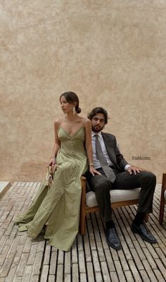 a man and woman sitting next to each other on a wooden bench in front of a wall