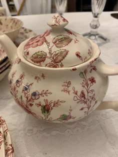 a white tea pot sitting on top of a table next to plates and cups with spoons