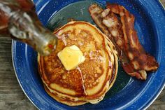 pancakes and bacon on a blue plate with syrup being drizzled over them