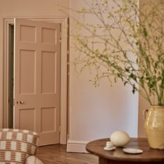 a vase with flowers sitting on top of a wooden table next to a chair and door