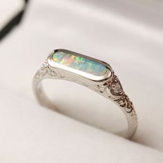 an opal and diamond ring sits on a white surface