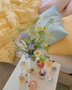 a white table topped with lots of bottles and vases filled with flowers next to a bed