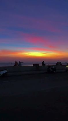 the sun is setting over the ocean and people are riding their bikes