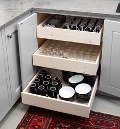 an open cabinet with plates and bowls in the bottom drawer, next to a rug