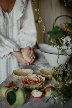 a woman in white shirt sitting at table with pies and apples on it's counter