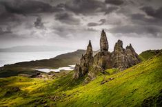 some very tall rock formations in the middle of a green field with water and mountains behind them