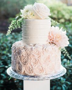 a wedding cake with white frosting and pink flowers on top is sitting on a clear pedestal