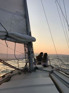 two women sitting on the bow of a sailboat in the ocean at sunset or dawn