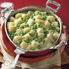 a pot filled with peas and dumplings on top of a wooden table next to a red plate