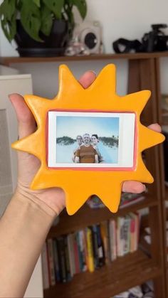 a person holding up a yellow sun shaped photo frame