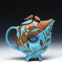 a blue and brown teapot with two birds on it's top sitting on a stand