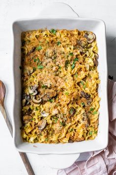 a casserole dish filled with pasta, mushrooms and parmesan cheese on a white surface