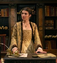 a woman standing in front of a desk with books on the shelves behind her and an open bookcase