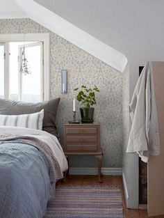 a bed sitting under a window next to a wooden table with a potted plant on it