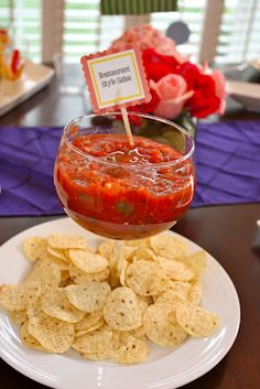 a white plate topped with chips and salsa next to a glass filled with red sauce