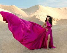 a woman in a pink dress is posing for a photo on the desert with mountains in the background