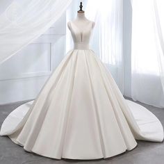 a white ball gown on display in front of a window with curtains and drapes