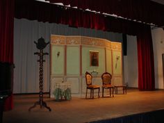 two chairs sitting in front of a stage with red curtains on the walls and floor