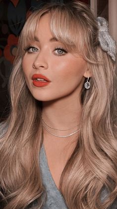 a woman with long blonde hair wearing a gray shirt and silver necklace, posing for the camera