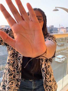 a woman standing on top of a balcony holding her hand up in the air with both hands