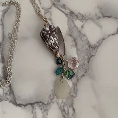 a sea shell is hanging from a silver chain on a marble counter top with beads and charms