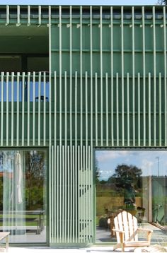 a cat sitting on the window sill of a green building with vertical slats covering it's windows