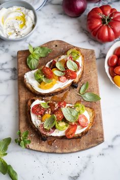 two pieces of bread with tomatoes, basil and mozzarella on them sitting on a cutting board