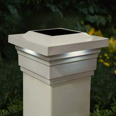 a white light that is on top of a planter in the grass with flowers behind it