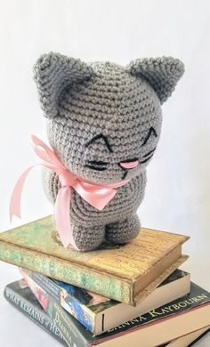 a crocheted cat sitting on top of books with a pink bow around its neck