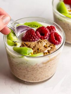 a person is spooning into a dessert with fruit and cream in it on a white surface